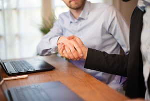 Image de deux personnes se serrant la main devant leurs ordinateurs afin d'illustrer notre article intitulé "Comment remporter des marchés publics efficacement"